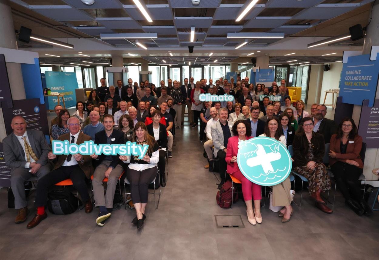 A group of people seated in a room holding signs that say biodiversity and climate.