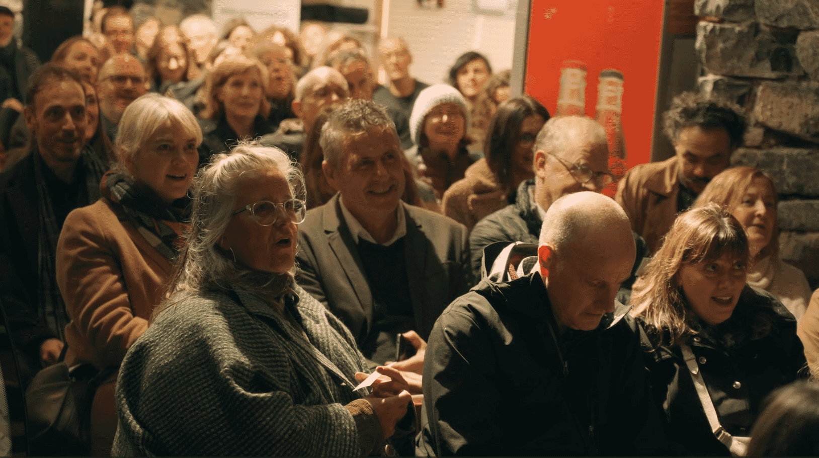 A group of people sit and stare at a stage ahead behind the camera