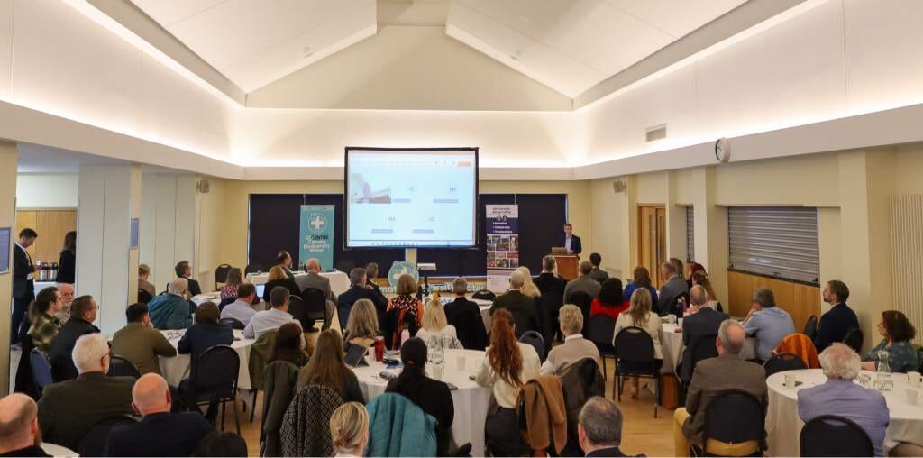A large crowd of people gathered in a spacious hall, engaged in conversation and looking at a whiteboard.